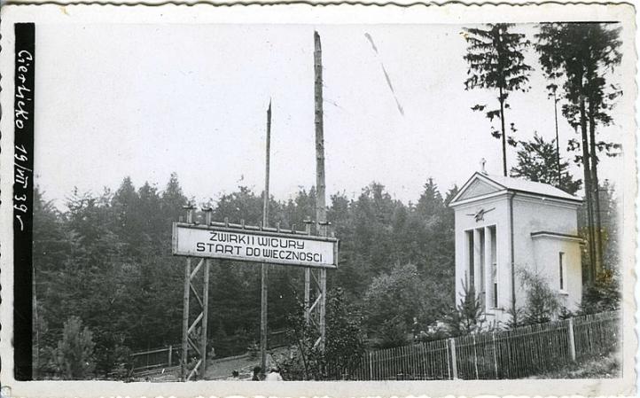 Widok ogólny Żwirowiska w Cierlicku, 19.07.1939, w tle widoczne dwa ułamane drzewa, tzw. maszty śmierci, i bramka z napisem 'Start do wieczności' (fot. wg fotografii nieznanego autora, za polonika.pl)