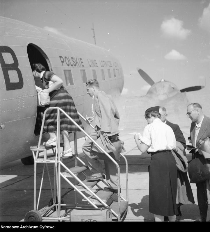 Przygotowania samolotu do wylotu w Porcie Lotniczym Warszawa-Okęcie. Pasażerowie wchodzący do samolotu. Widoczna stewardessa kontrolująca bilety, 1955 r. (fot. Narodowe Archiwum Cyfrowe)
